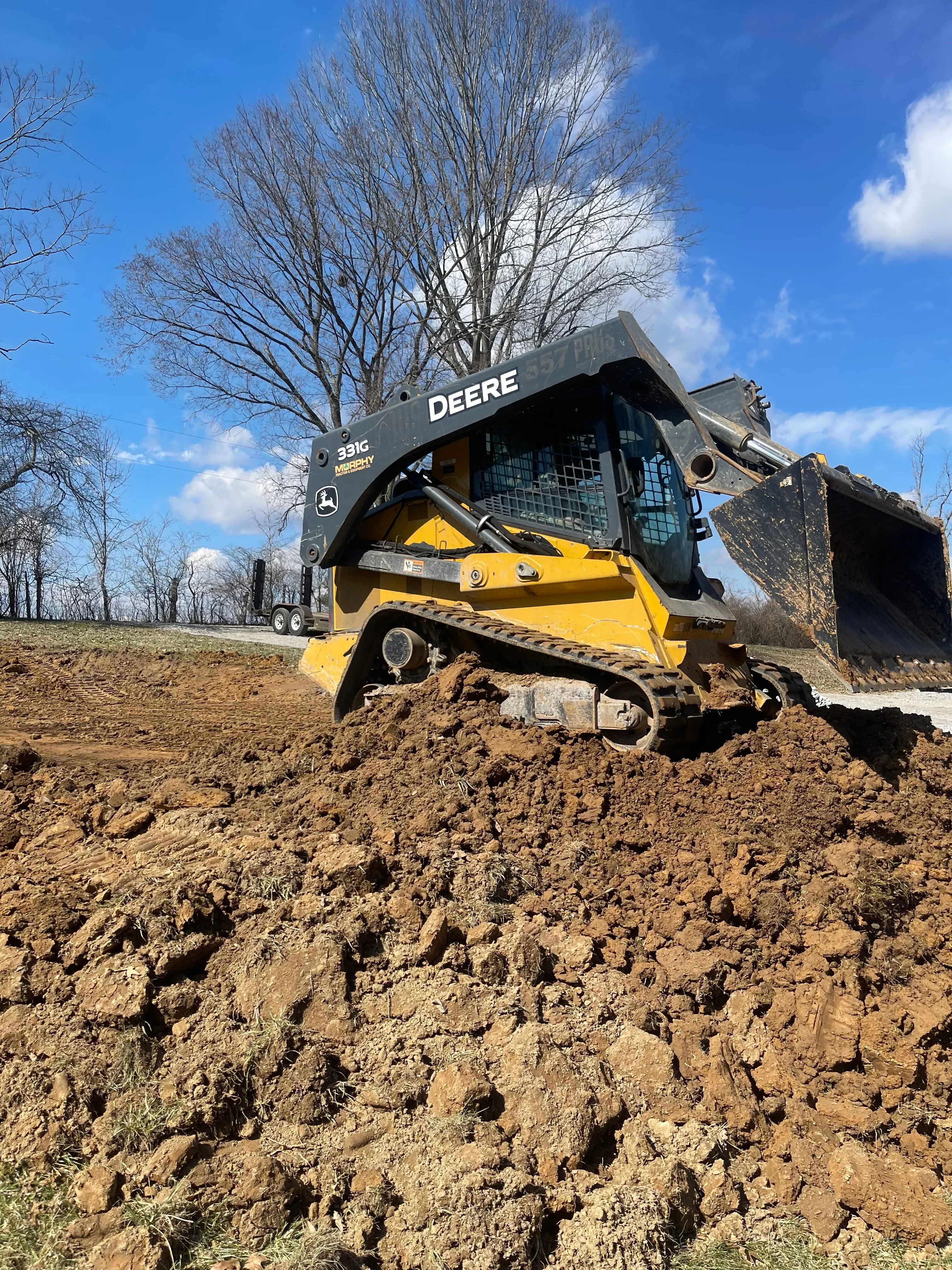 Yellow skid steer loader with bucket excavating compacted soil material on residential site