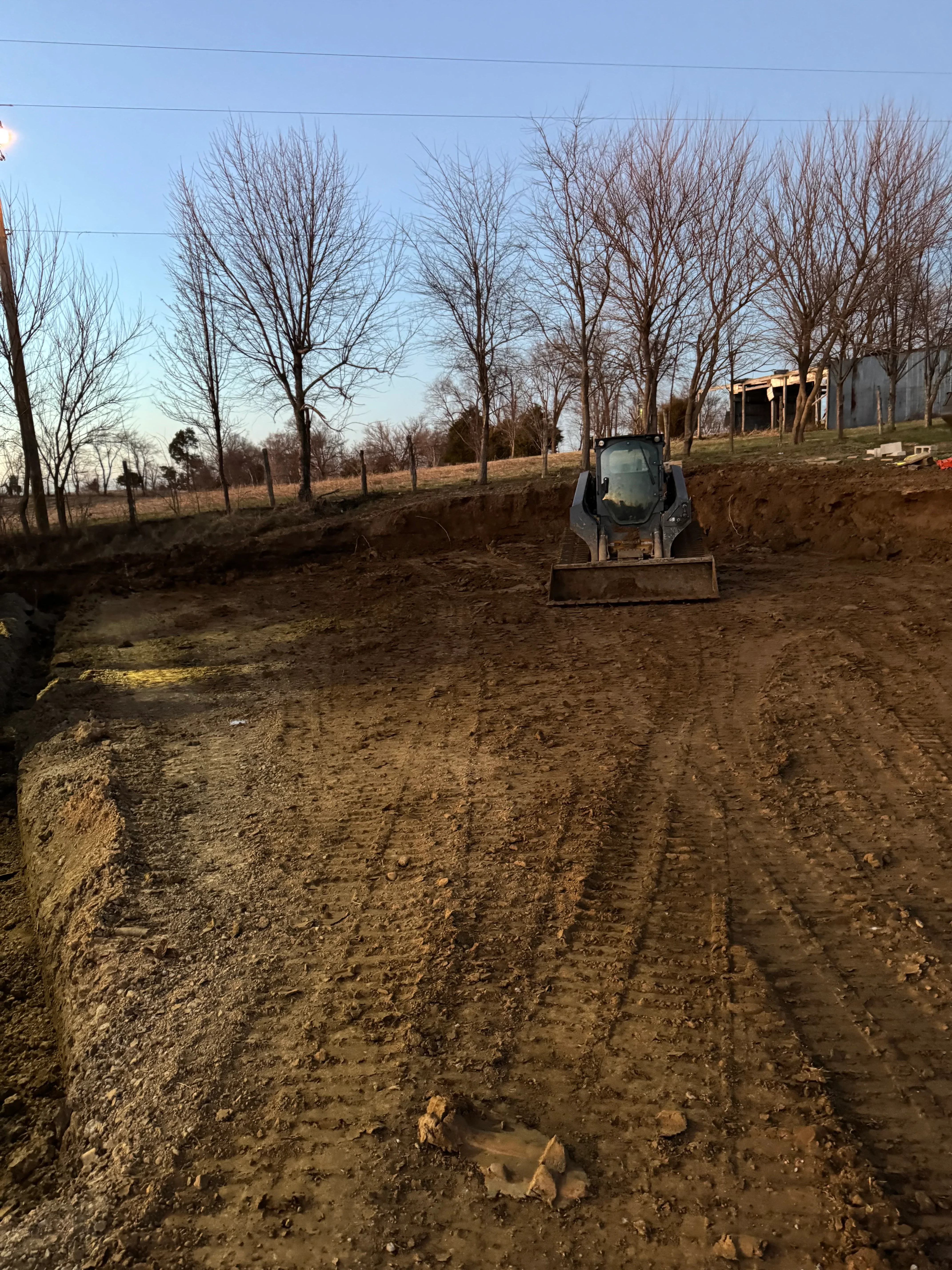 Excavated driveway site with graded soil and heavy equipment during site preparation