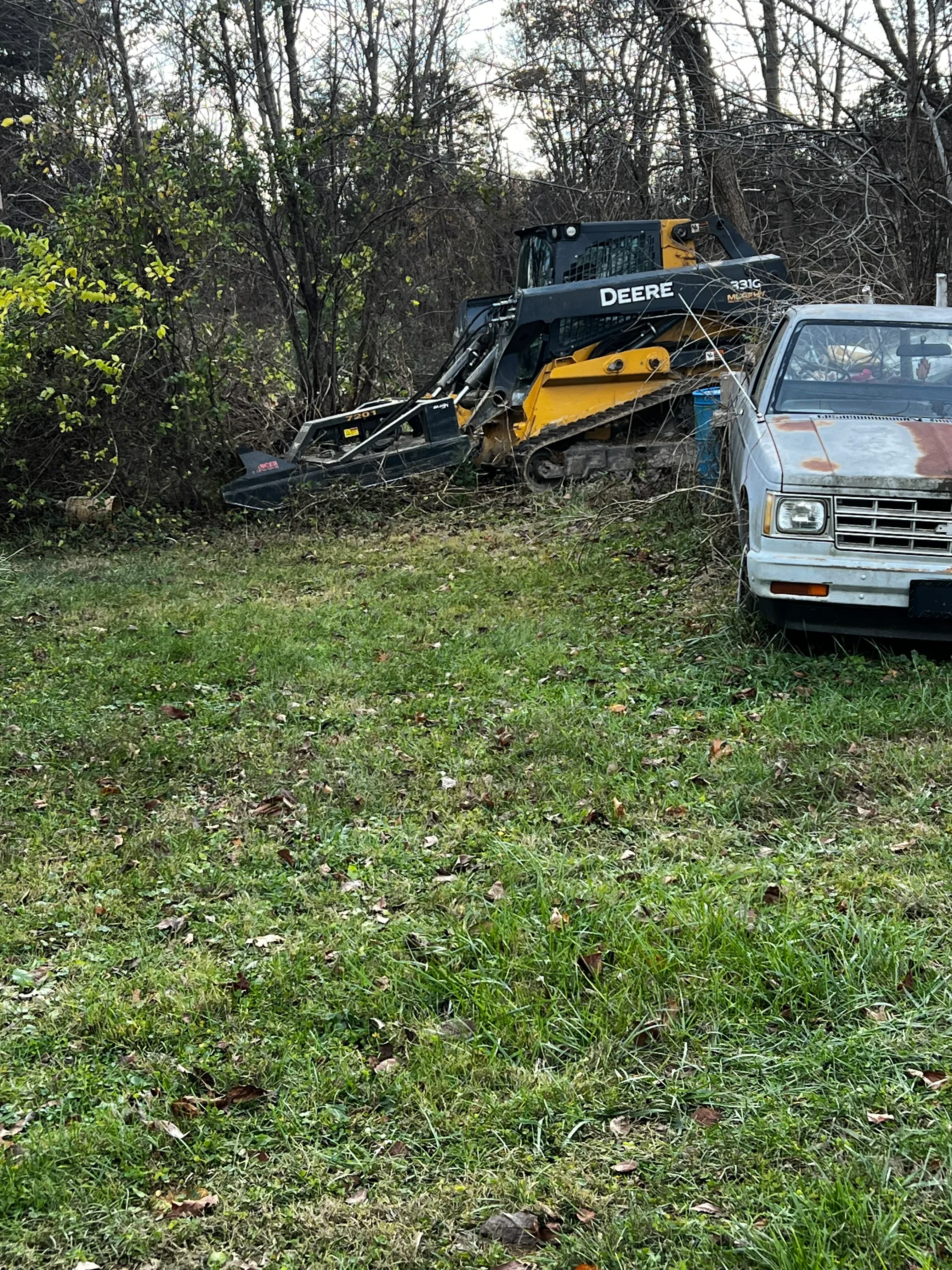 John Deere compact track loader clearing overgrown vegetation and brush from residential property