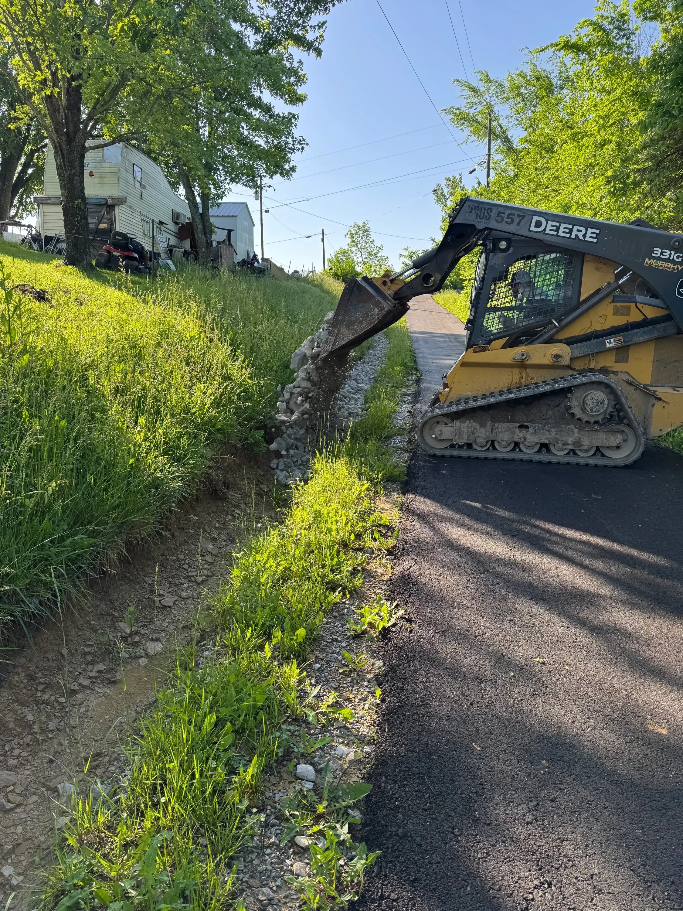 Skid steer loader excavating driveway with crushed stone base and cleared vegetation