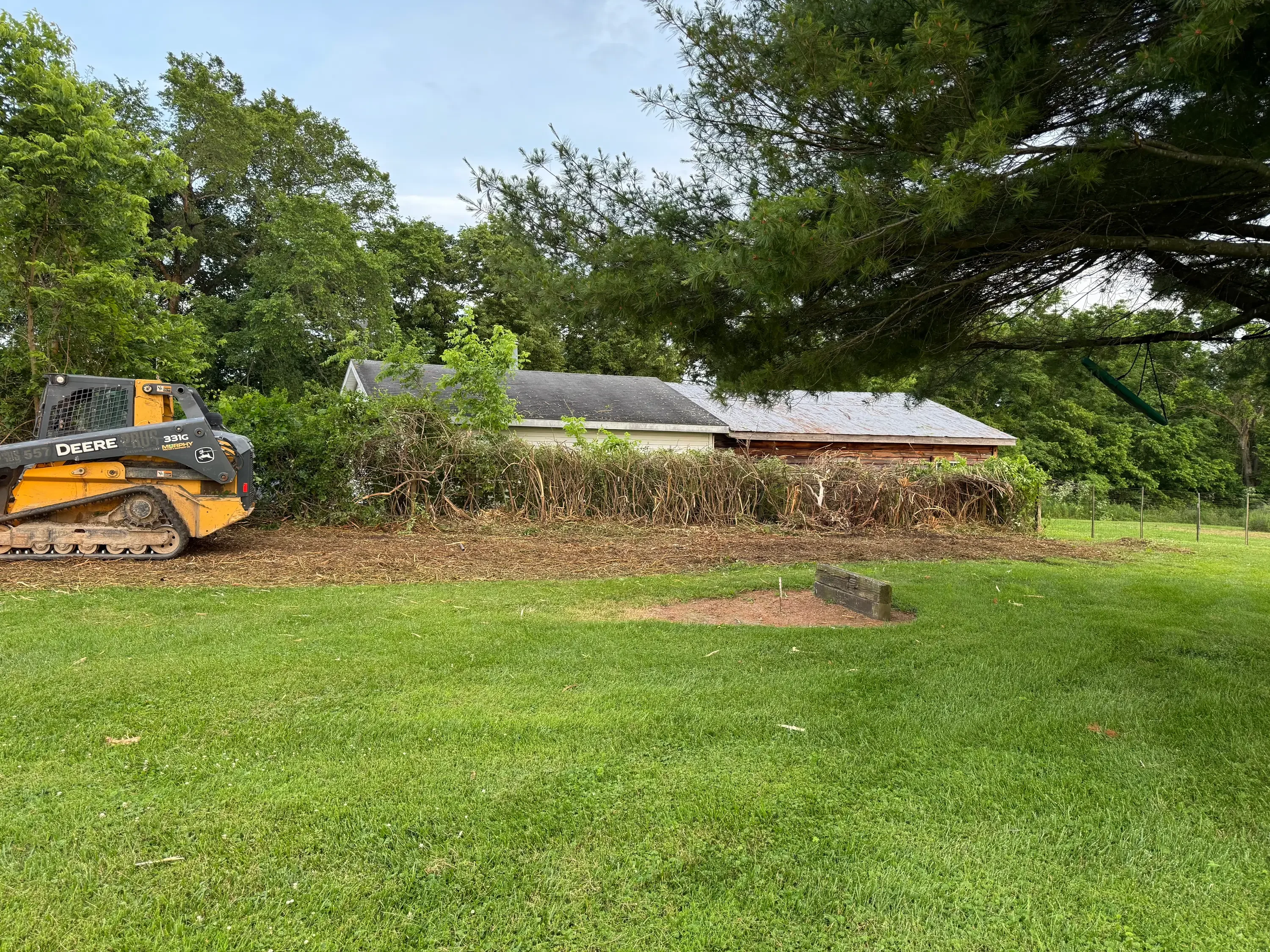 Deere track loader clearing brush and vegetation from residential property with cleared ground visible