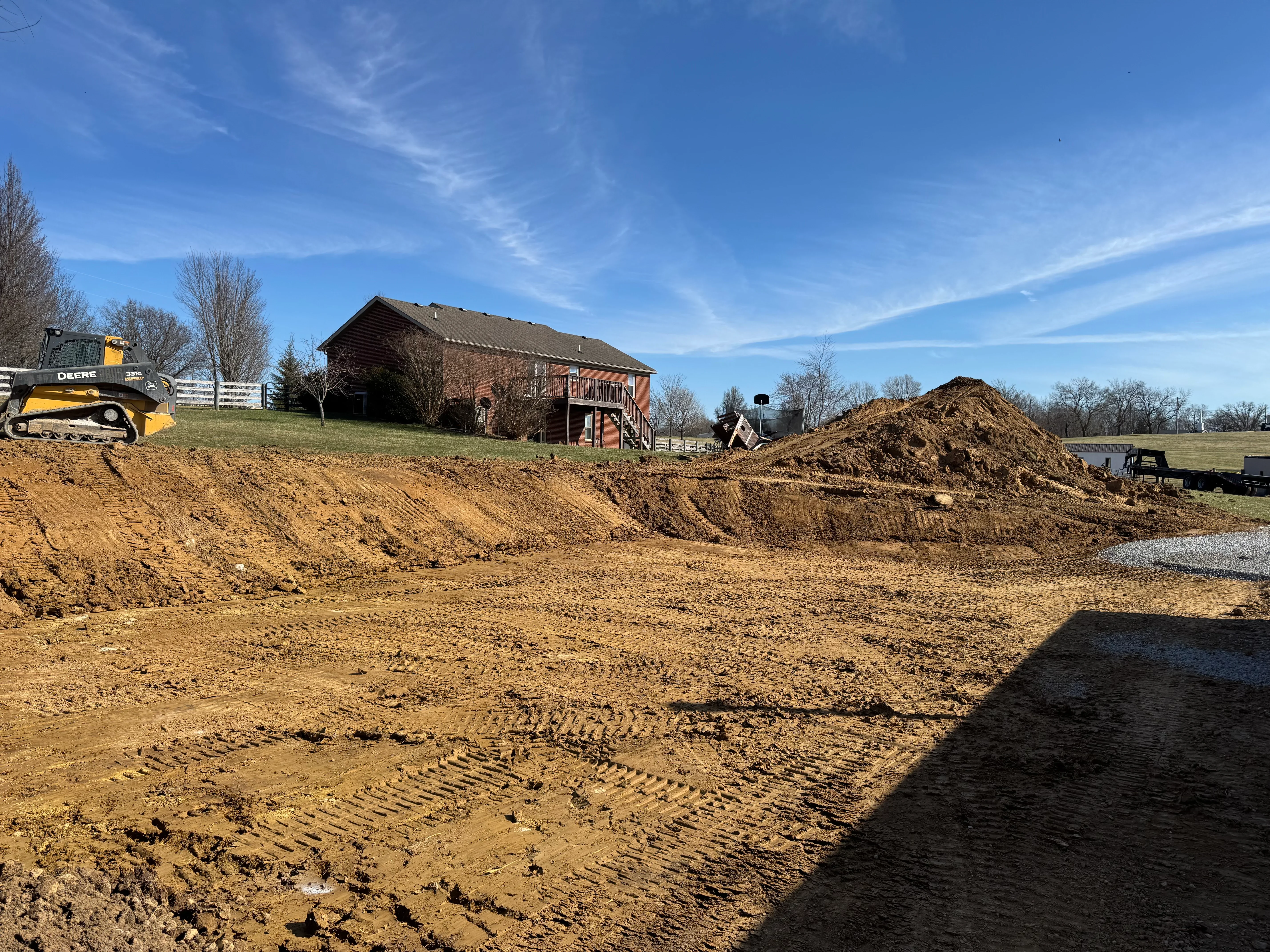 Excavated residential lot with graded soil, equipment, and material stockpiles